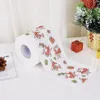 A roll of toilet paper with a Christmas theme, featuring Santa Claus and gift patterns, is placed on a white surface next to a small decorative Christmas tree and gift boxes. Náhľad obrázku produktu