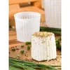 A cheese mold and a finished cheese on a wooden surface with herbs and chives. Produktbild-Vorschau