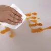 A hand is wiping a spill on a textured white surface with a paper towel. Voir les images du produit