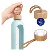 A hand holding a light blue water bottle with a bamboo lid and a brown rope handle. The image also shows a close-up of the bamboo lid and a separate shot of the lid's interior. Náhľad obrázku produktu