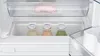 Close-up view of the interior of a refrigerator, showing a crisper drawer with food items and a storage bin with bottles. Produktbild-Vorschau
