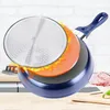 A cross-section of a blue frying pan with layers highlighted and flames around it, suggesting heat and cooking. The background shows a kitchen counter and a brick wall. Produktbild-Vorschau