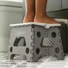 A child's feet are standing on a gray folding stool in a bathroom. Náhled obrázku produktu