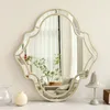 A decorative mirror is displayed on a white surface with a few decorative items in the foreground and background. Produktbild-Vorschau