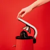 A hand is shown pressing down on the lever of a red citrus juicer against a red background. Podgląd zdjęcia produktu