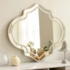 A decorative mirror is displayed on a white surface, reflecting a room with curtains and lamps. Produktbild-Vorschau