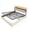 A white upholstered bed frame with a metal mattress support mechanism raised, showing the storage space underneath. The headboard has integrated LED lighting and a padded section that can be folded down. Anteprima dell’immagine prodotto