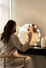 A woman is applying makeup in front of a lighted vanity mirror. Produktbild-Vorschau