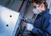 A person wearing safety gear is drilling into a metal object. Voir les images du produit