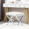 A white upholstered stool with a silver metal frame is placed on a white fluffy rug in front of a white vanity table. Produktbild-Vorschau