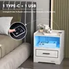 A white nightstand with LED lighting and a drawer, placed next to a bed. The image highlights the charging capabilities of the nightstand. Produktbild-Vorschau