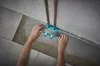 A person is using a tile laying tool to apply adhesive to the floor around pipes. Produktbild-Vorschau