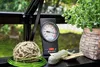 A thermometer and gardening supplies are on a shelf in a greenhouse. Produktbild-Vorschau