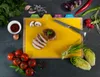 A top-down view of a kitchen cutting board with various ingredients and a knife. Anteprima dell’immagine prodotto