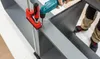 A person is using a drill to assemble a gray shelving unit, with a red clamp holding parts together. Produktbild-Vorschau