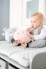 A baby is sitting on a changing mat with two plush toys. Náhľad obrázku produktu
