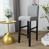 A light gray bar stool with a fabric cover is shown in a room with a gold side table and a bouquet of flowers. Produktbild-Vorschau