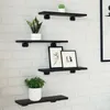 Four black wooden shelves are mounted on a white brick wall, each displaying decorative items. Produktbild-Vorschau