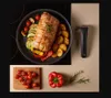 A cooked meal with roasted meat and vegetables in a pan, alongside fresh ingredients and a kitchen utensil. Voir les images du produit