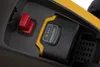 A close-up view of the battery compartment of a lawnmower, showing the battery, a red safety switch, and a battery charge indicator. Produktbild-Vorschau