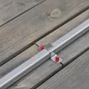 A close-up view of a metal bracket with red fasteners attached to a silver bar, which is resting on weathered wooden planks. Produktbild-Vorschau
