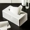 A white tissue box with tissues inside, placed on a black tiled surface. Produktbild-Vorschau