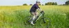 A man is riding an electric bicycle through a grassy field on a sunny day. Produktbild-Vorschau
