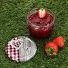 A jar of strawberry jam with strawberries and the lid on a grassy surface. Anteprima dell’immagine prodotto