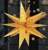A golden, star-shaped paper lantern with cut-out stars is illuminated from within, hanging in front of a dark background with bokeh lights. Anteprima dell’immagine prodotto