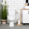 A clean and modern bathroom setting with a white toilet, a wooden toilet paper holder, and a tall green plant. Náhled obrázku produktu