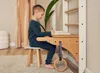 A young boy is sitting at a wooden desk attached to a white wall-mounted climbing frame, drawing in a book. Produktbild-Vorschau