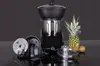 A food processor and its accessories are displayed on a reflective black surface against a dark gray background. A pineapple and a small melon are placed to the right of the food processor. Produktbild-Vorschau