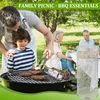 A family is having a picnic and BBQ in a park. A father is grilling burgers with his son, while other family members are sitting at a table in the background. A smoking tube is placed on the grill. Produktbild-Vorschau