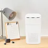 A white air purifier sits on a wooden desk next to a desk lamp and a calendar. Podgląd zdjęcia produktu