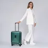 A woman in a white suit stands next to a green suitcase. Podgląd zdjęcia produktu