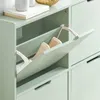 A close-up view of a green shoe cabinet with one of the flip-out drawers open, revealing two beige shoes inside. Produktbild-Vorschau