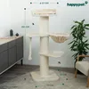 A cream-colored cat tree with multiple levels, scratching posts, and toys, set up in a room with a cabinet and a plant. Podgląd zdjęcia produktu