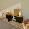 A modern living room scene featuring a lowboard TV cabinet with open doors, displaying books and decorative items. A lamp, vase, and artwork are also visible. Voir les images du produit