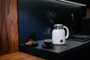 A kitchen counter scene with a white electric kettle, a cup of coffee, and a croissant. Podgląd zdjęcia produktu