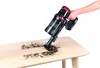 A hand holding a black and red cordless vacuum cleaner is shown cleaning dirt off a wooden table. Produktbild-Vorschau