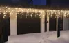 Icicle lights are hung on the eaves of a house above a garage and two doors, with snow on the ground. Produktbild-Vorschau