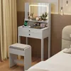 A white vanity table with a lighted mirror and a stool, set up in a bedroom next to a bed and curtains. Podgląd zdjęcia produktu