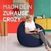 A woman sits on a navy blue beanbag chair in a colorful room, writing in a notebook. Anteprima dell’immagine prodotto