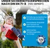 A young girl is happily swinging on a red swing seat attached to a wooden swing set. The background shows trees and foliage, suggesting an outdoor setting. A blue overlay box contains text and a TÜV SÜD logo, highlighting safety features. Produktbild-Vorschau