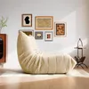 A beige beanbag chair is placed on a rug in a well-lit room with several framed pictures on the wall. Produktbild-Vorschau