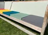Several colorful cushions are placed on a wooden bench outdoors, with grass in the foreground. Náhled obrázku produktu