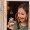A young girl is holding a small snow globe with a bear inside, looking at it with a smile. The background is dark with bokeh lights. Produktbild-Vorschau