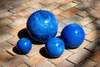 Four blue ceramic spheres of varying sizes are arranged on a paved outdoor surface. Produktbild-Vorschau