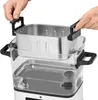 Hands are shown placing a stainless steel steaming basket into a clear plastic container, which is part of a larger appliance. Produktbild-Vorschau