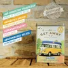 A vintage-style tin box featuring a VW bus and camping scene, set against a brick wall and wooden surface. Voir les images du produit